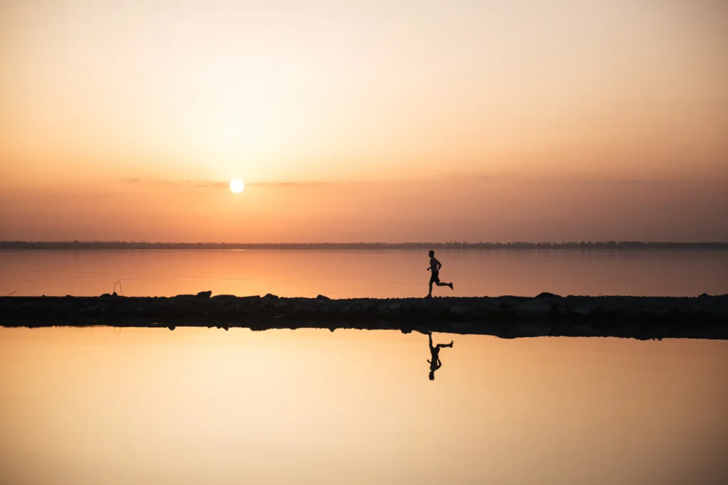夕陽下，一名跑者沿著湖岸奔跑，水面映出倒影。